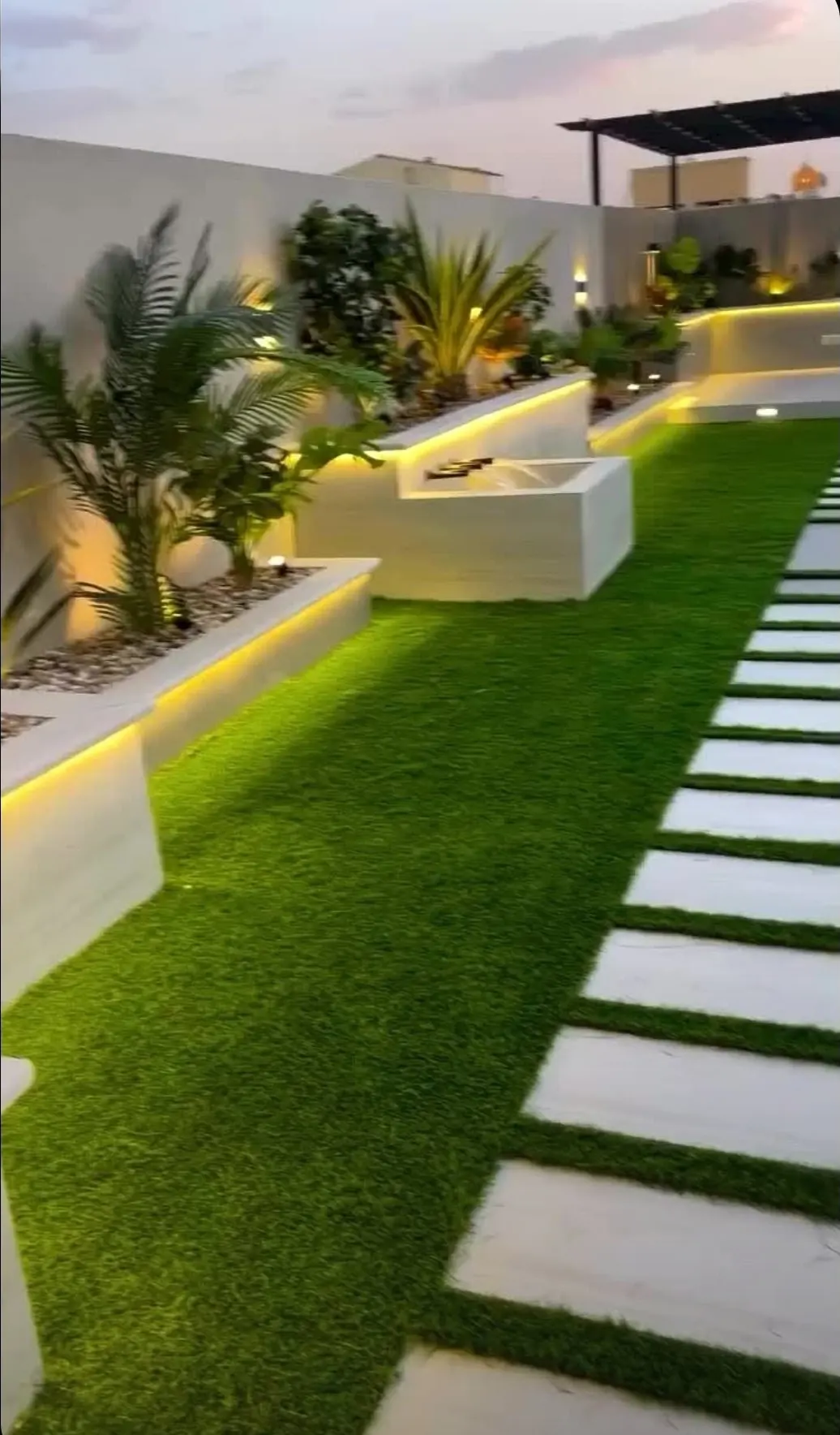 Modern lit walkway with planters, palms, and concrete-paver path on artificial turf